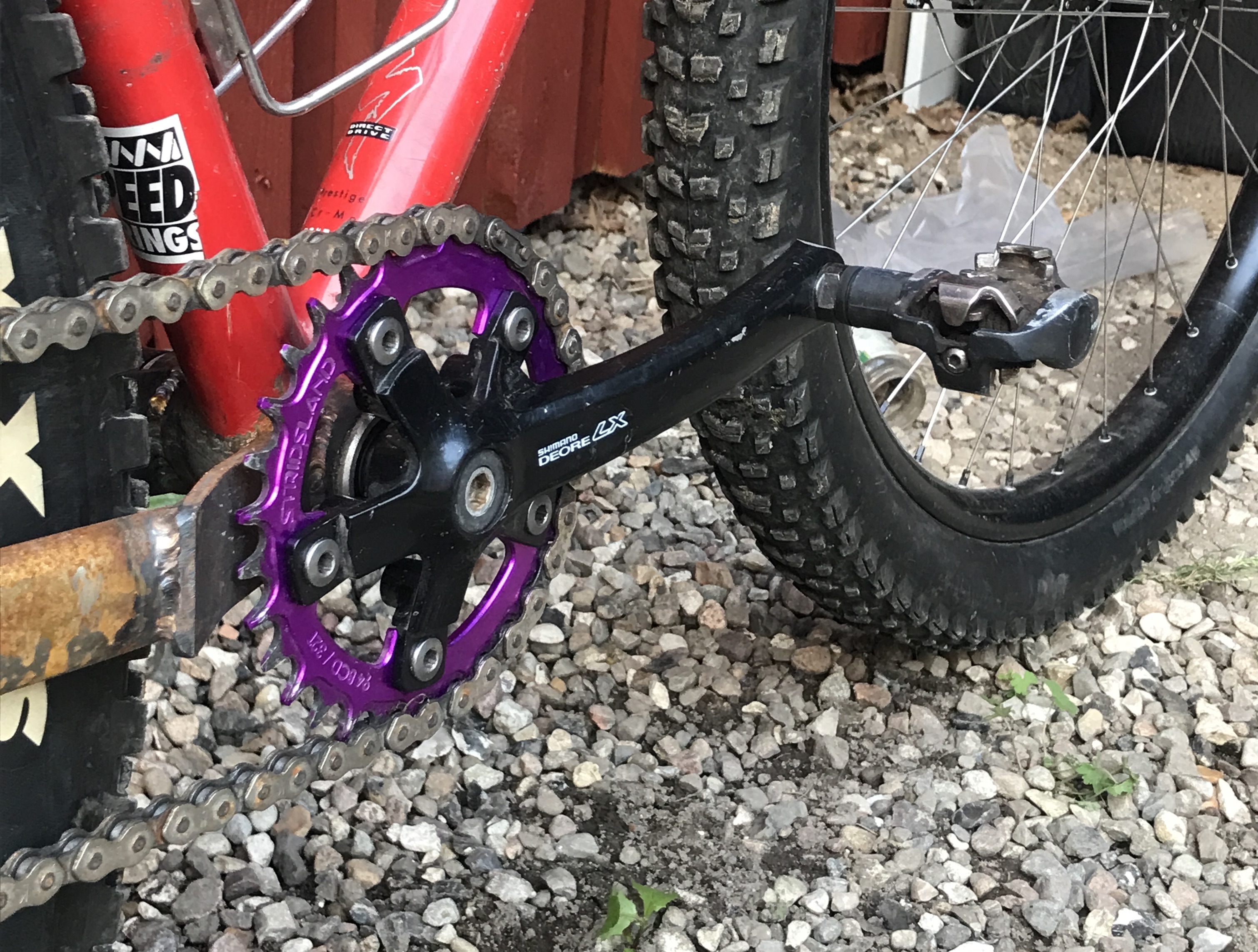 closeup of a red specialized mountain bike with a set of shortened 153mm shimano deore lx cranks in black with a purple stridsland chainring